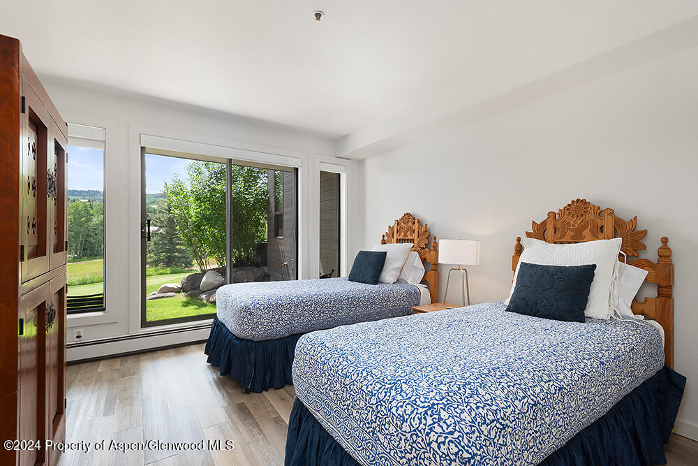 Bedroom with two blue-and-white patterned beds, carved wooden headboards, and large windows overlooking a green yard.