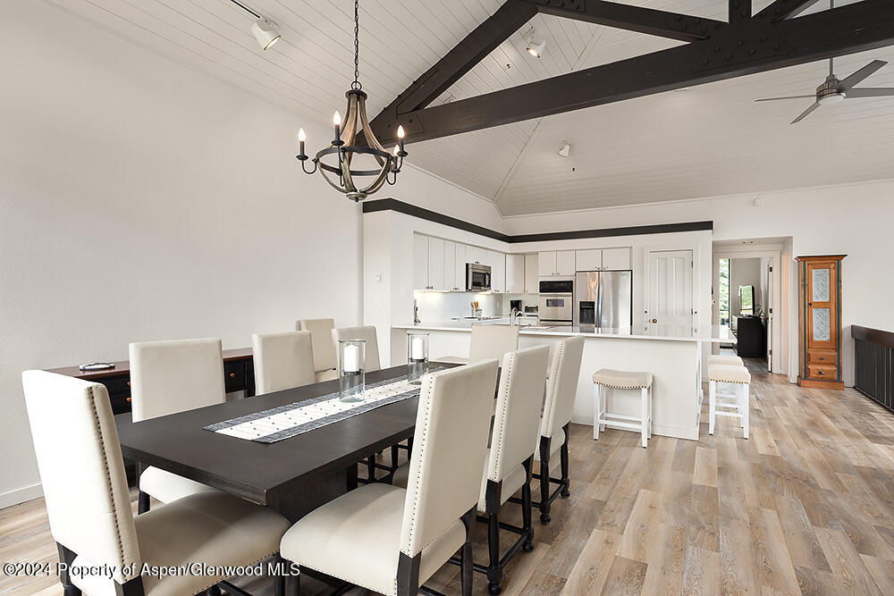 Open kitchen and dining area with a vaulted beamed ceiling, white island, and dark dining table.