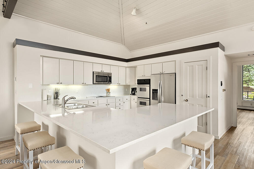 Modern white kitchen with a large island, stainless steel appliances, and vaulted ceiling.