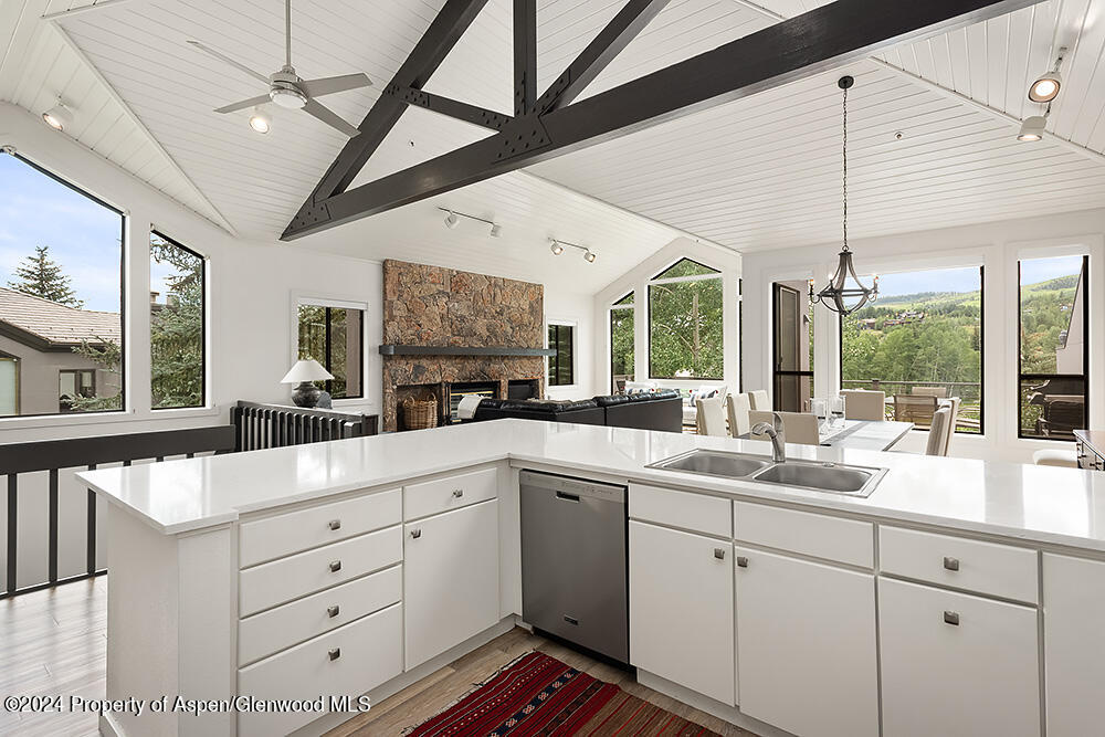 Open-plan kitchen with a large white island, exposed dark beams, and a stone fireplace beyond.