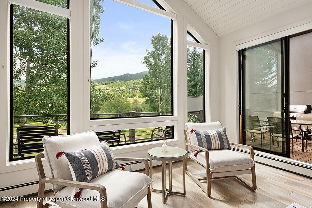 Bright sitting area with two armchairs and expansive windows overlooking trees and a mountain ridge.