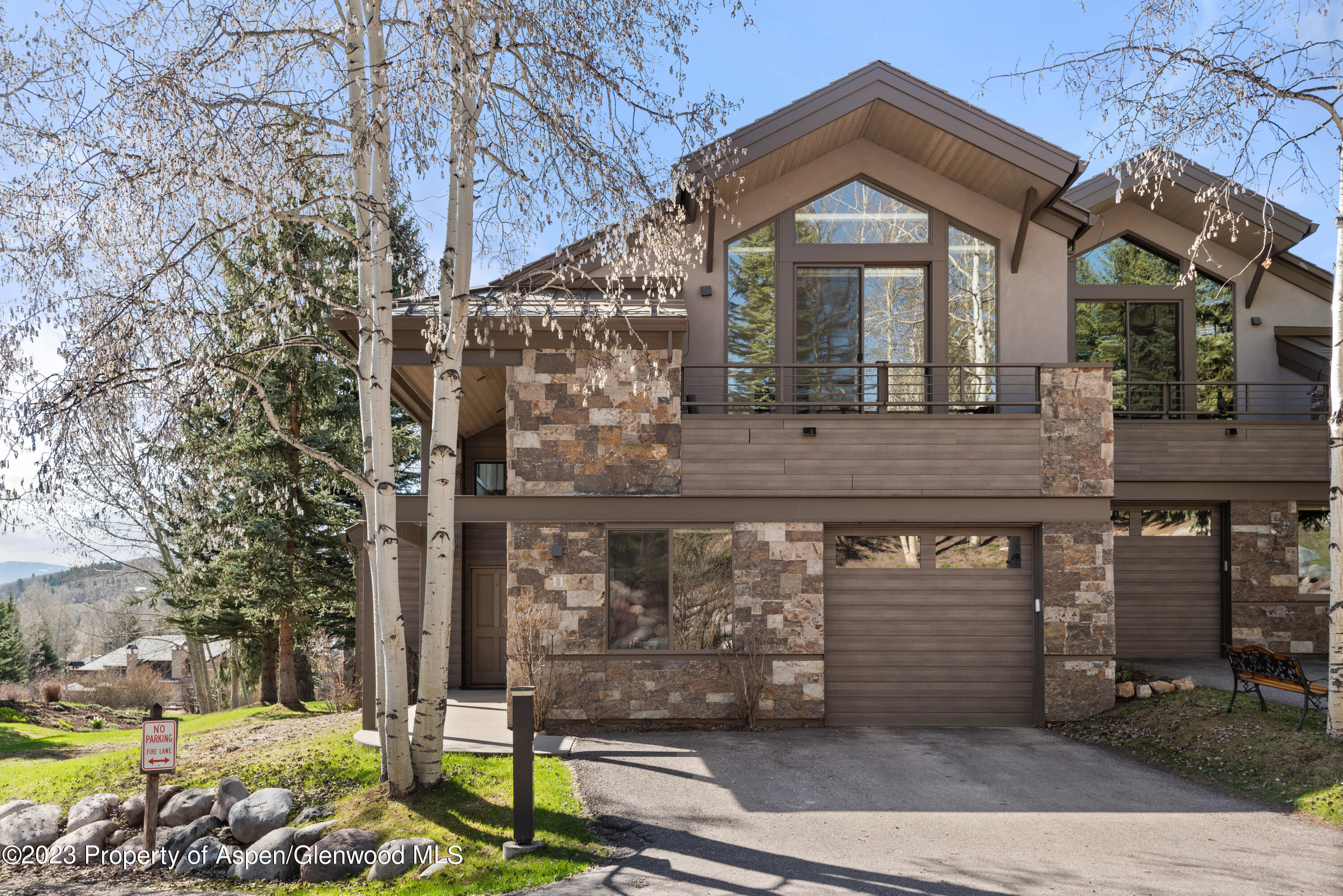 Modern stone-and-wood mountain home with large windows, garage, and aspens in front.