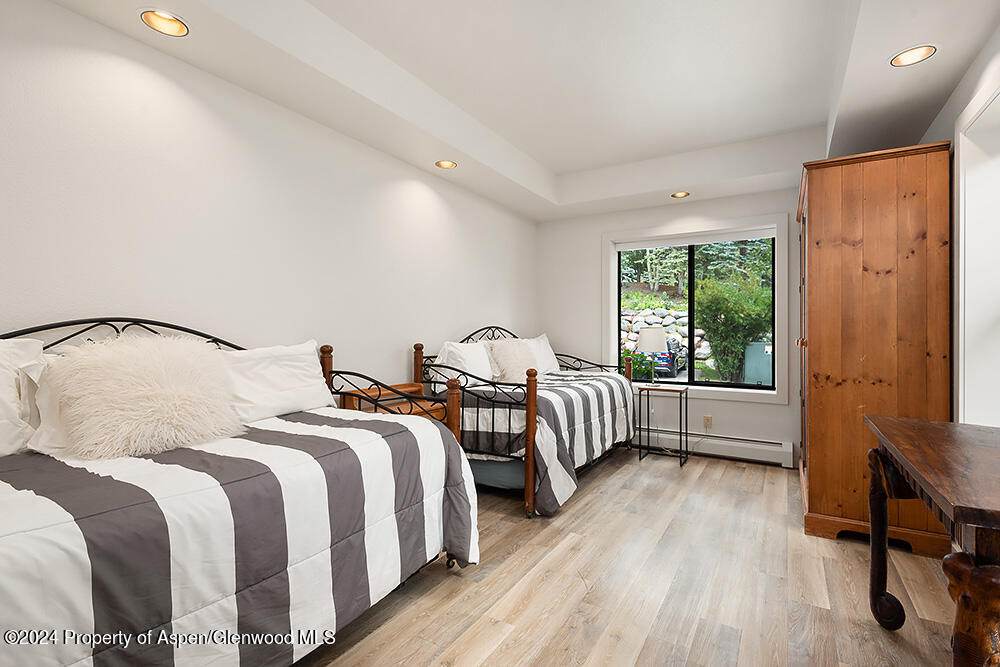 Bedroom with two striped beds, a tall wooden wardrobe, and a window overlooking greenery.