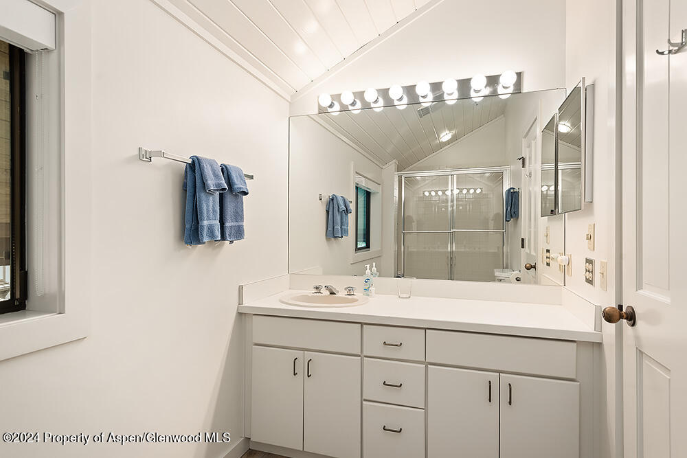 Bathroom vanity with a large lighted mirror, blue towels, and a glass-enclosed shower.