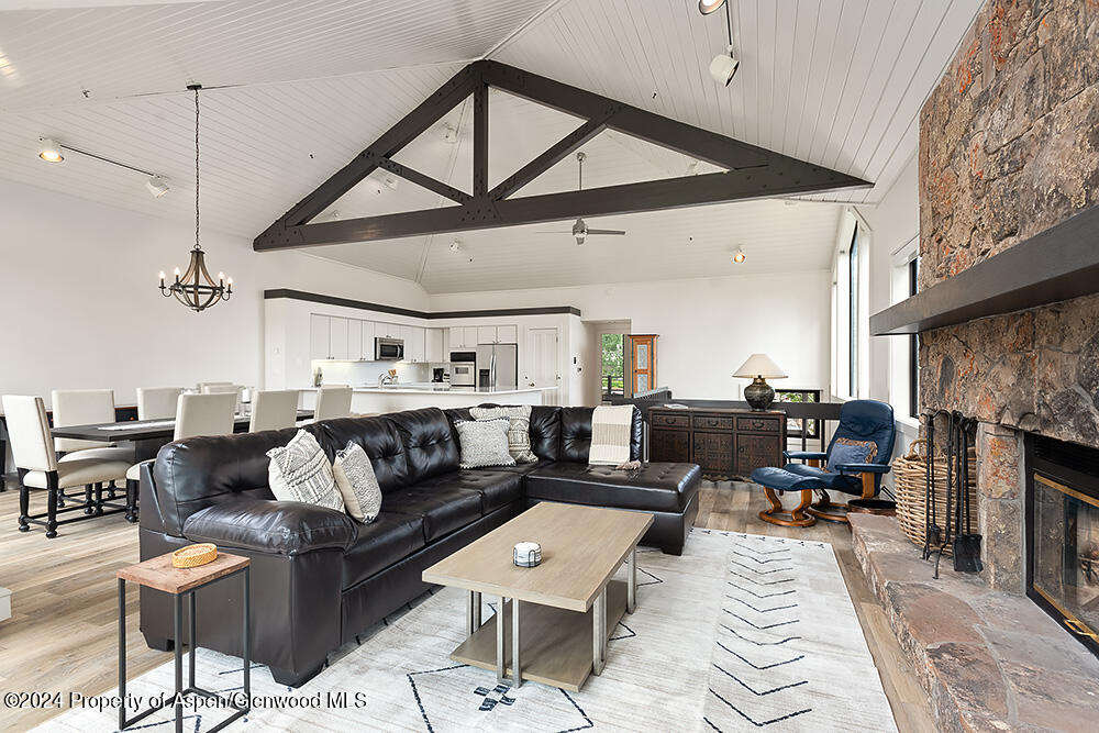 Open-plan living room with a black leather sectional, vaulted ceiling, and large stone fireplace.
