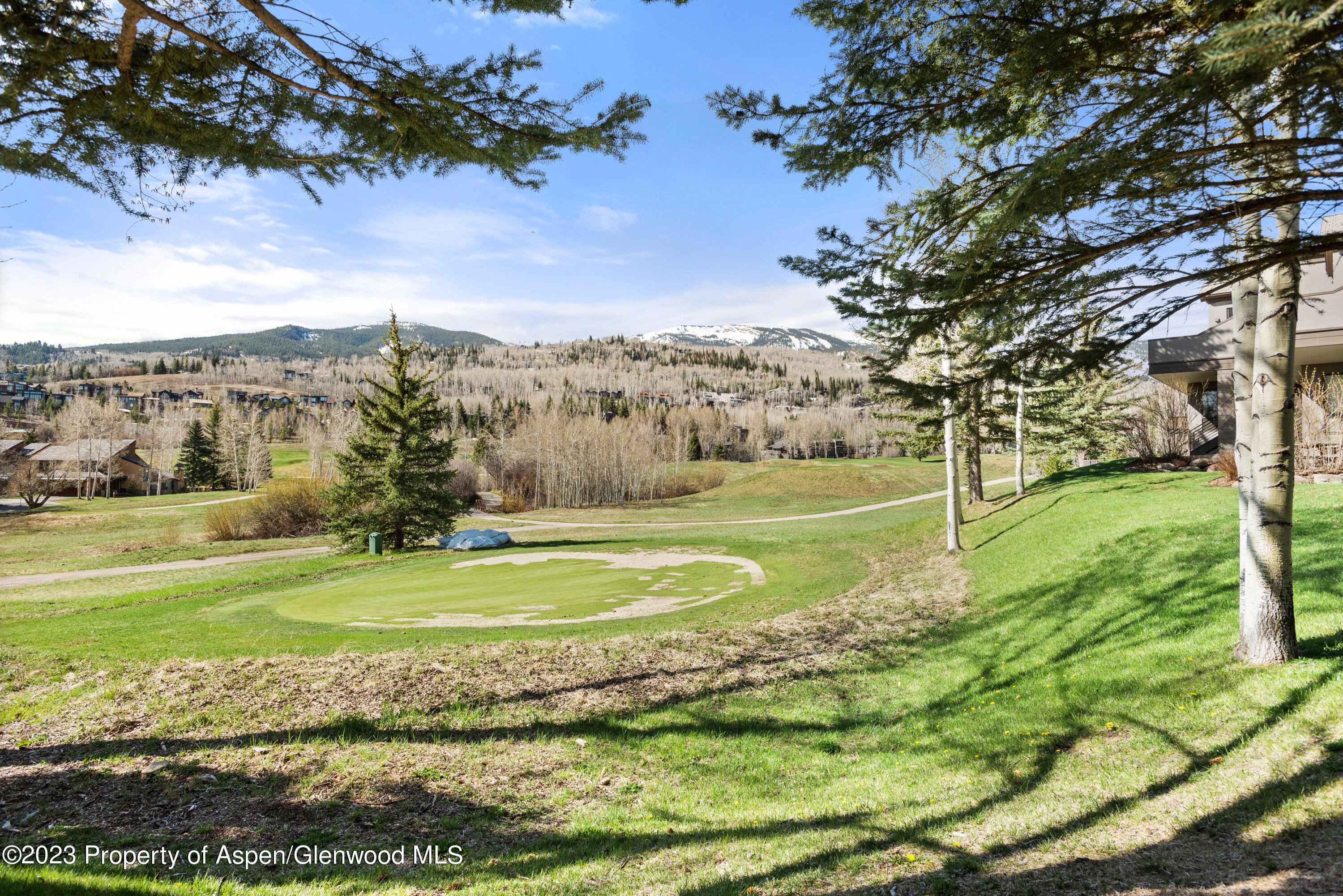 Landscaped grounds with a golf green, walking paths, and snow-dusted mountains beyond.