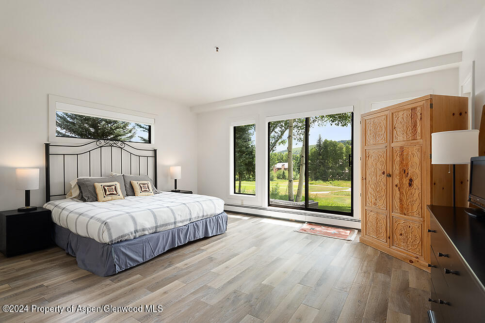 Bedroom with a king bed, carved wooden armoire, and sliding glass doors overlooking greenery.
