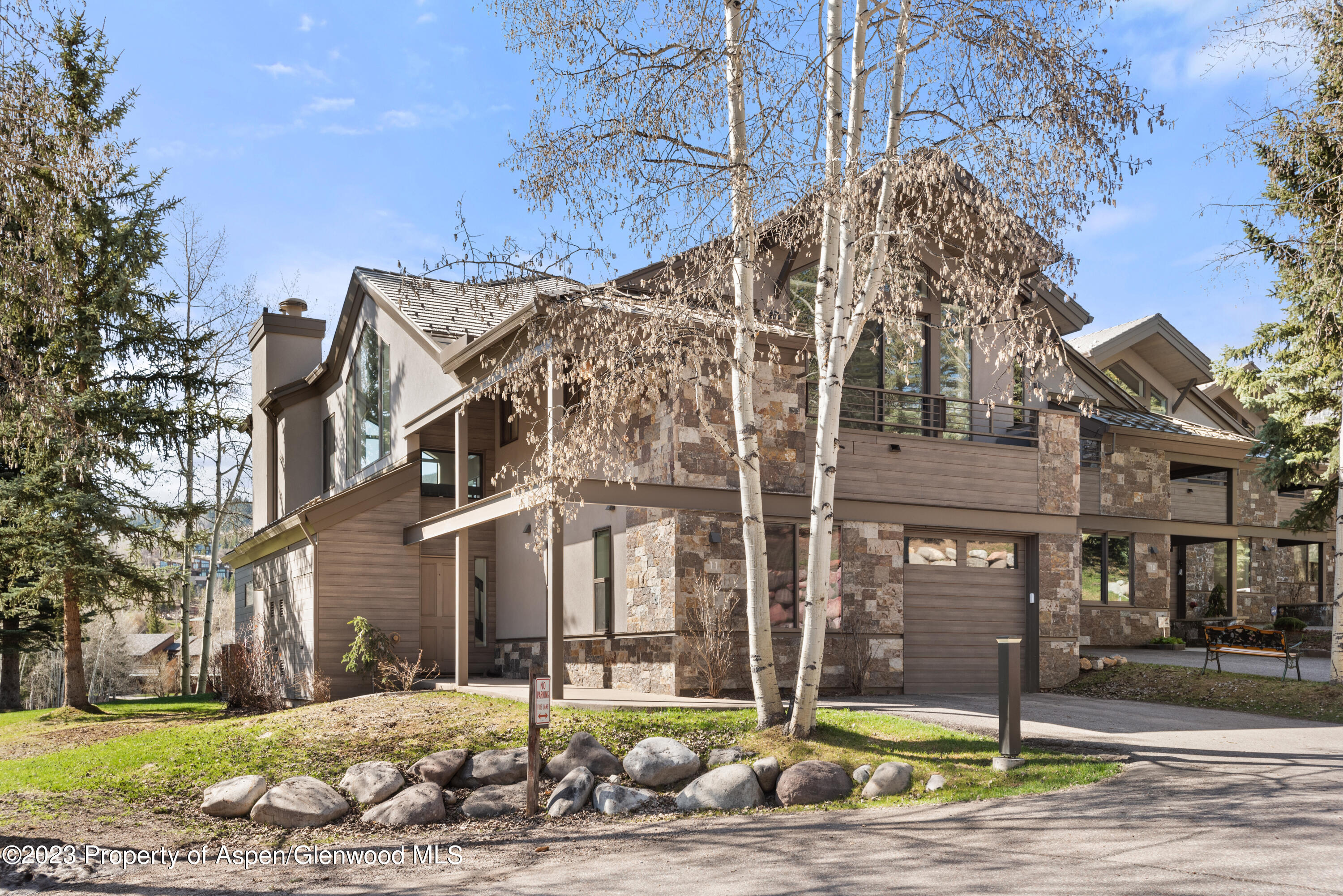 Modern mountain home with stone and wood siding, a balcony, garage, and aspens in front.