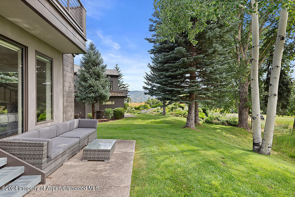 Patio with wicker seating beside a green lawn, mature trees, and distant mountains.