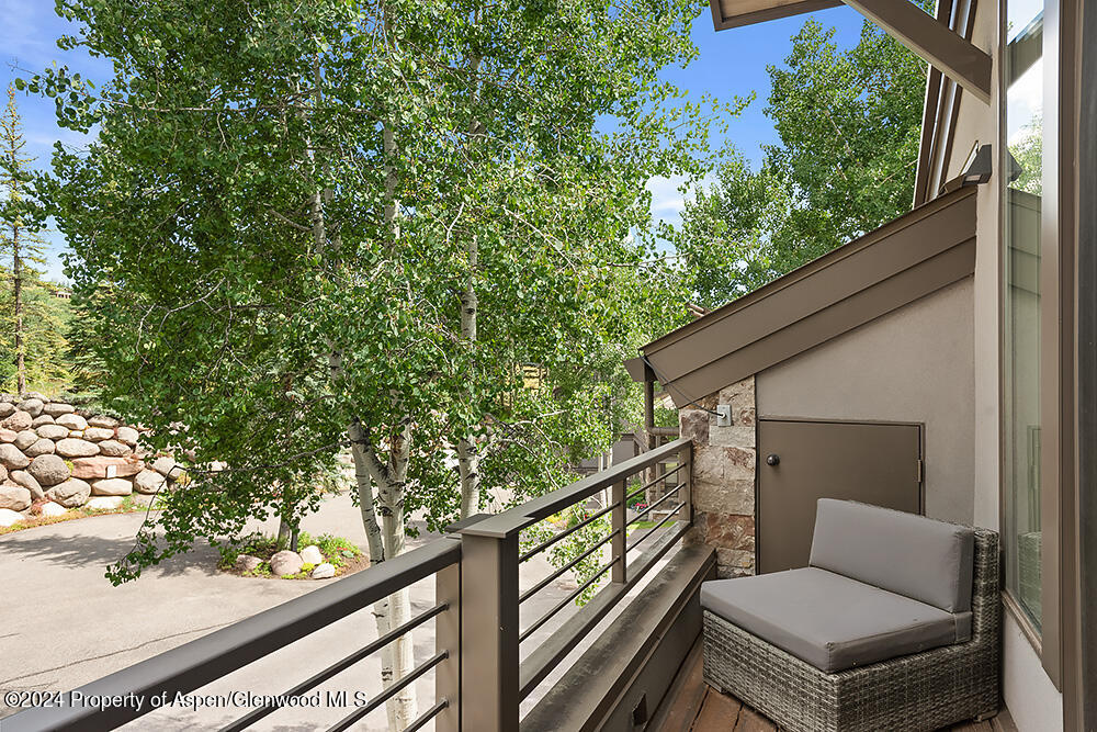Balcony with a wicker lounge chair, metal railing, and leafy aspen trees beyond.