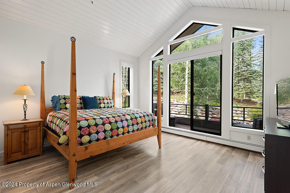 Bedroom with a wooden four-poster bed and tall windows overlooking trees.