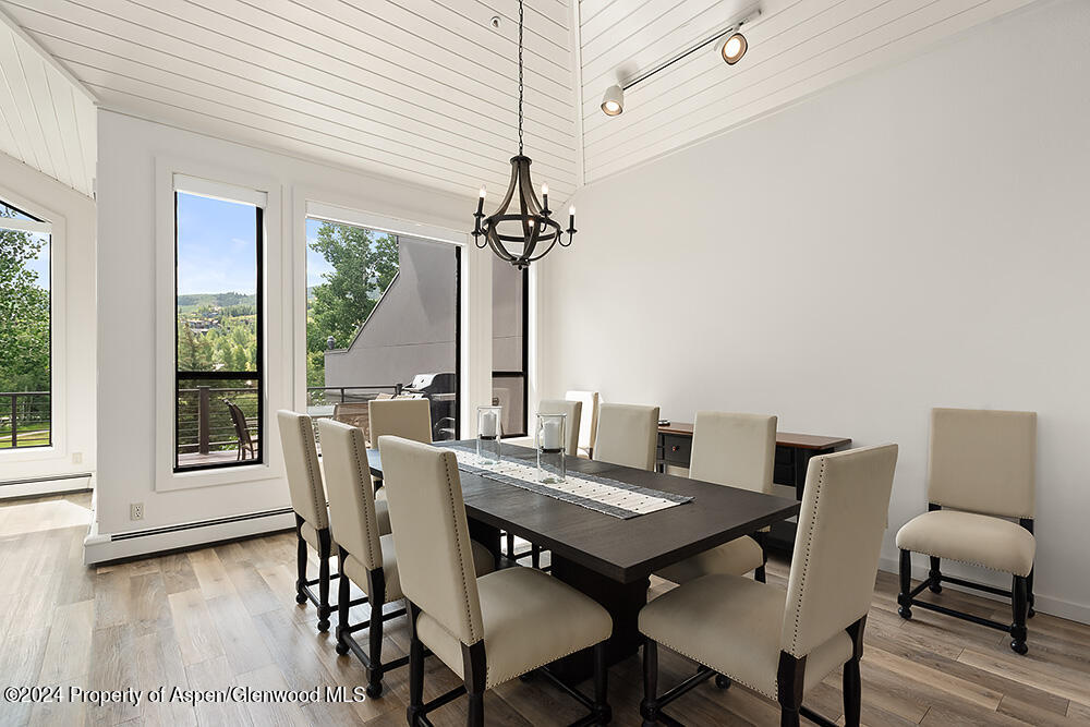Dining room with a dark table, cream chairs, vaulted ceiling, and tall windows overlooking greenery.