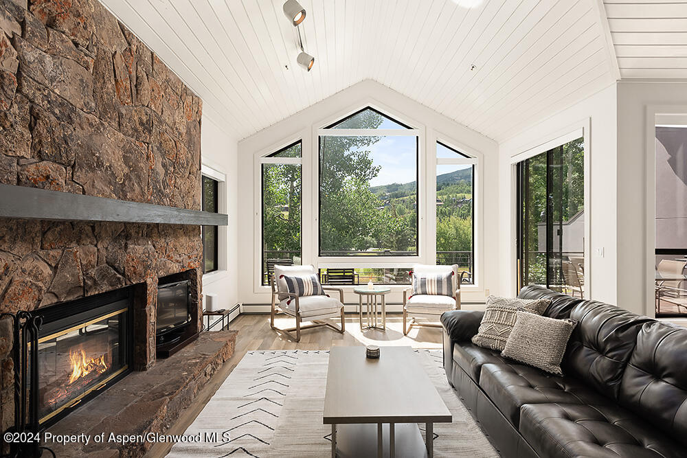 Living room with a stone fireplace, vaulted ceiling, and windows overlooking trees and a mountain.
