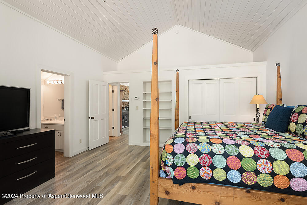 Bedroom with a wooden four-poster bed, colorful circular bedding, and a vaulted white ceiling.