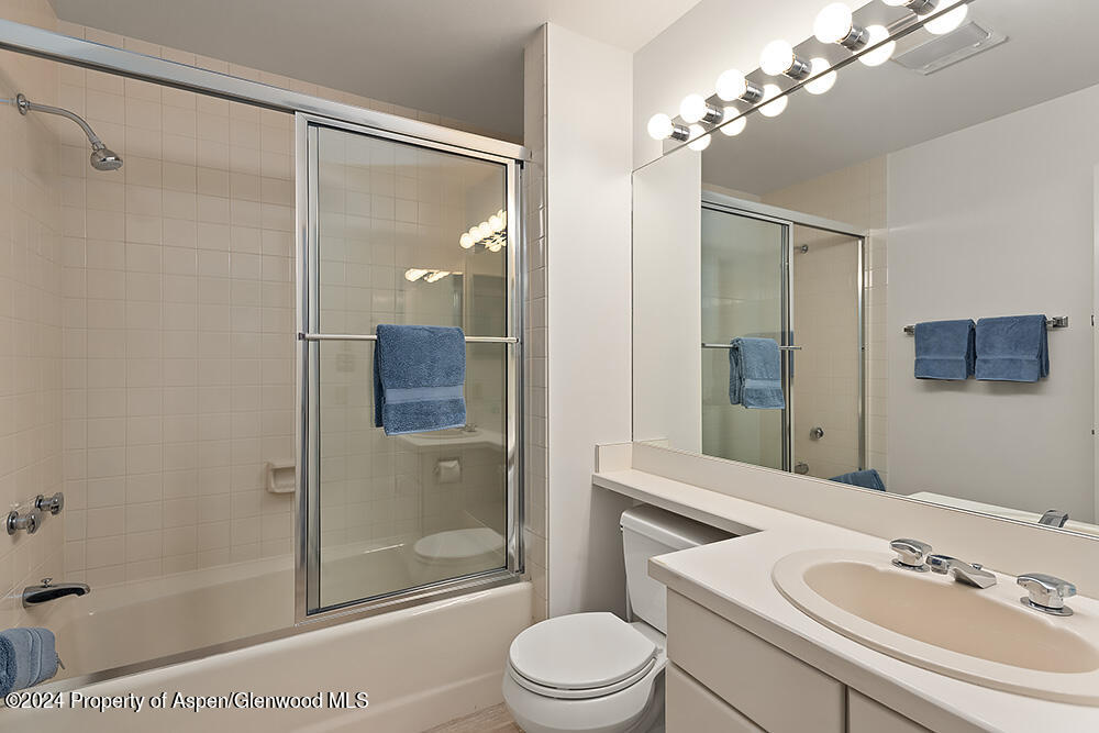 Bathroom with a glass shower enclosure, white vanity, large mirror, and blue towels.