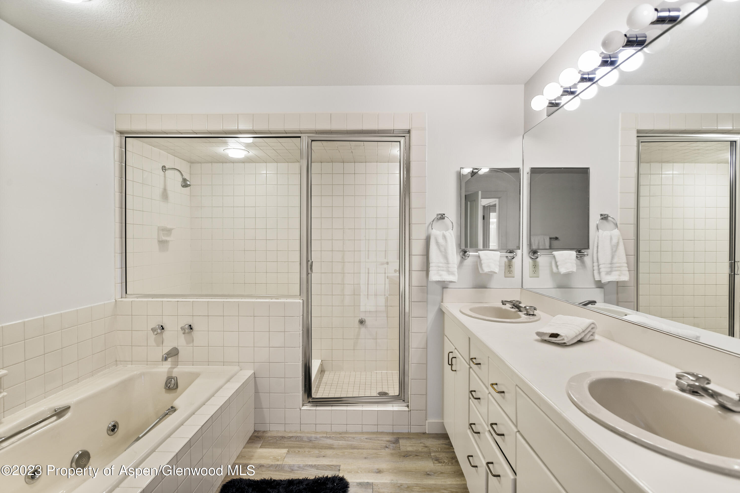 Bathroom with a tiled bathtub and glass shower beside a long double-sink vanity.