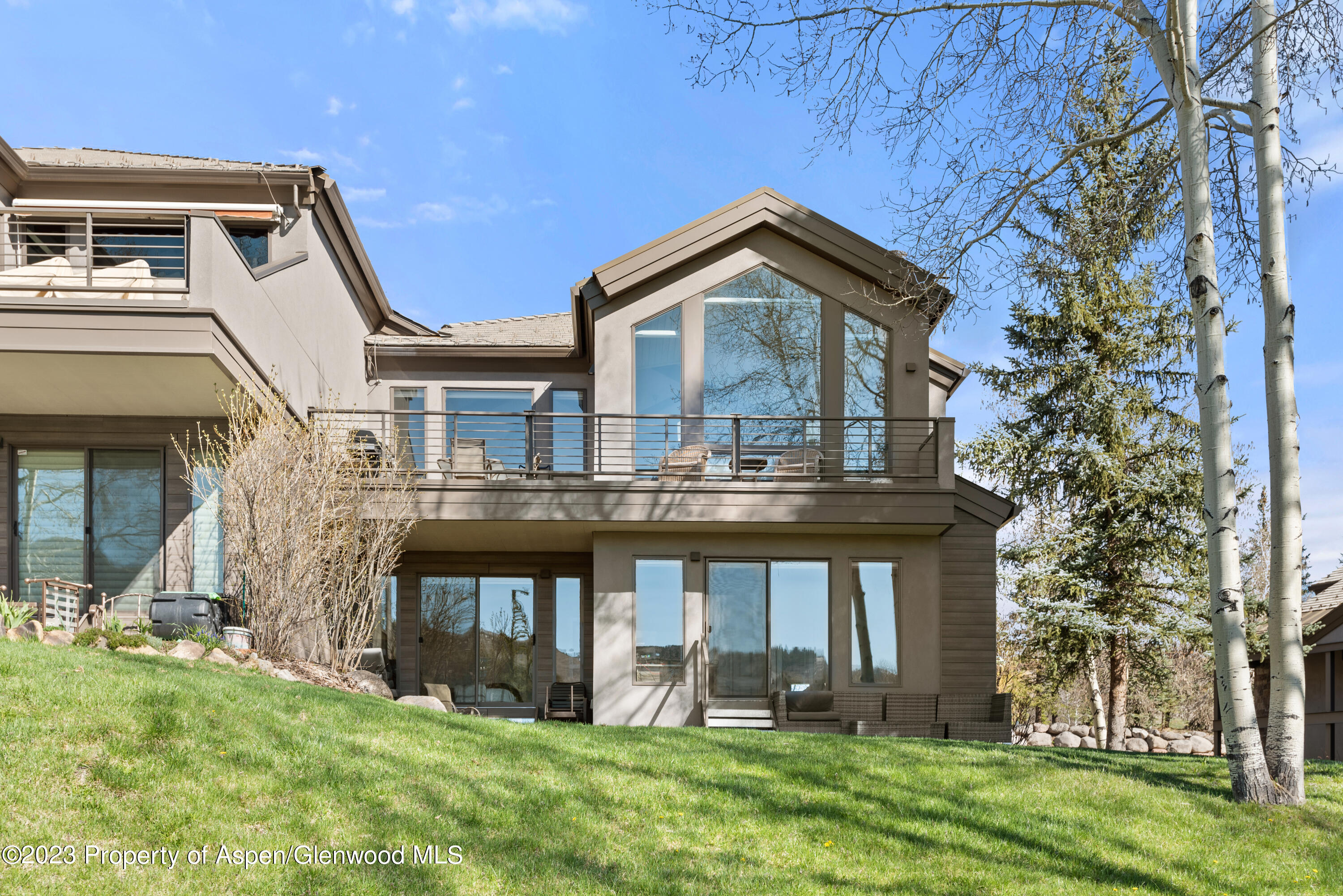 Modern multi-level home with a broad balcony, large windows, and a green lawn.