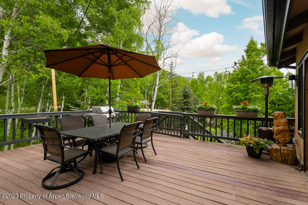 Outdoor deck with dining set and umbrella, overlooking leafy trees and a distant mountain.