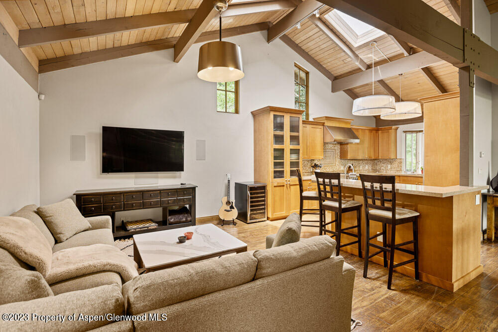 Open living room and kitchen with a vaulted timber ceiling, sectional sofa, and breakfast island.