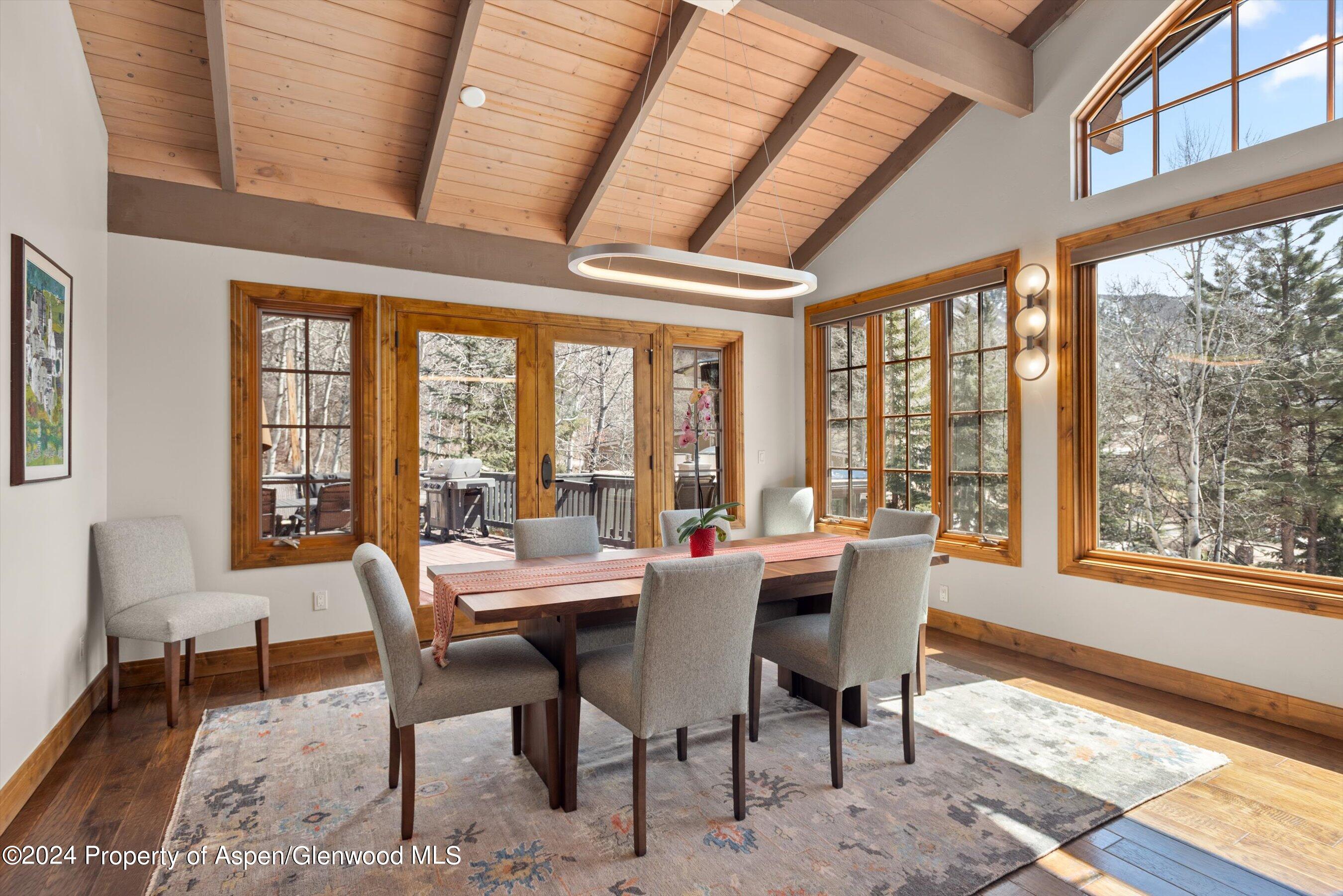 Dining room with a vaulted wood ceiling, large windows, and glass doors opening onto a deck.