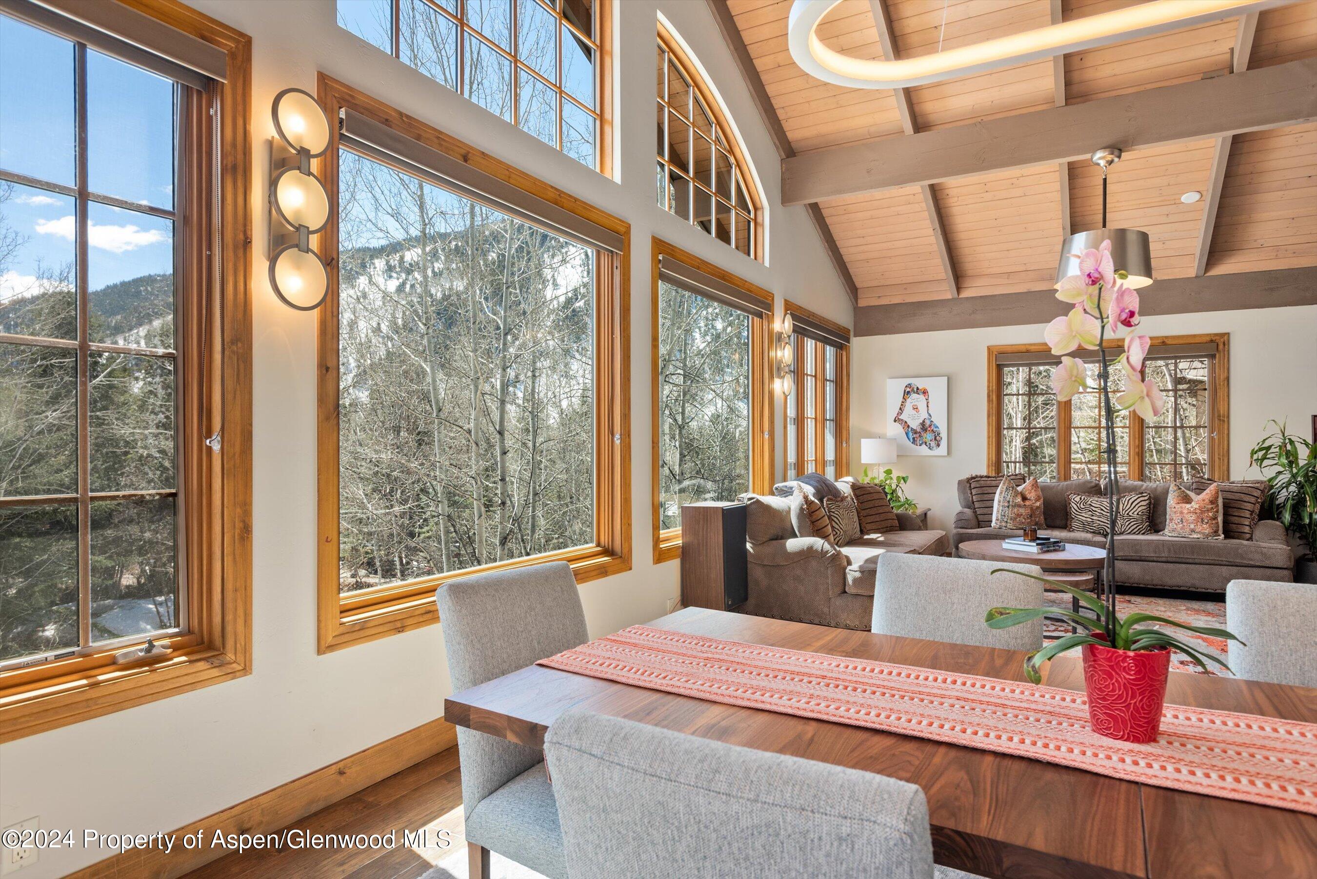 Dining and living area with vaulted wood ceiling, large mountain-view windows, and a wood dining table.
