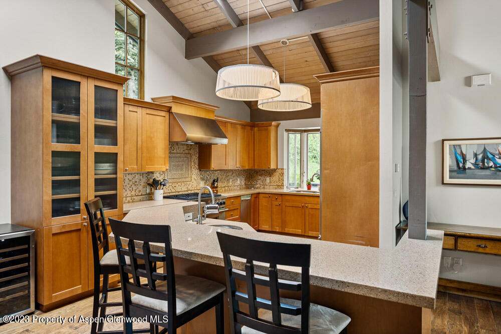 Kitchen with warm wood cabinetry, a large stone island, exposed timber ceiling, and pendant lights.