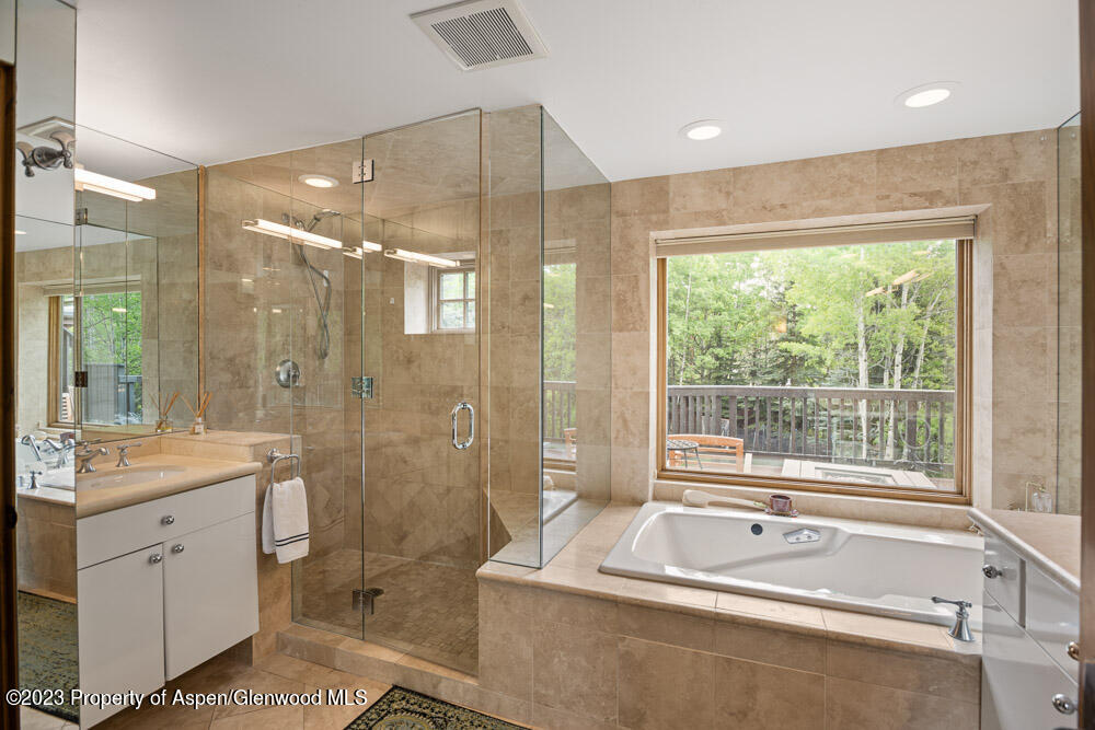 Tiled bathroom with a glass shower, built-in tub, and large window overlooking trees.