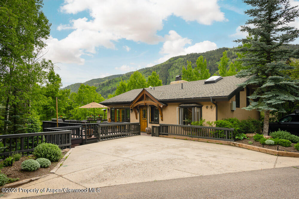 Aspen home with a broad driveway, raised deck, timber-trimmed entry, and wooded mountain backdrop.