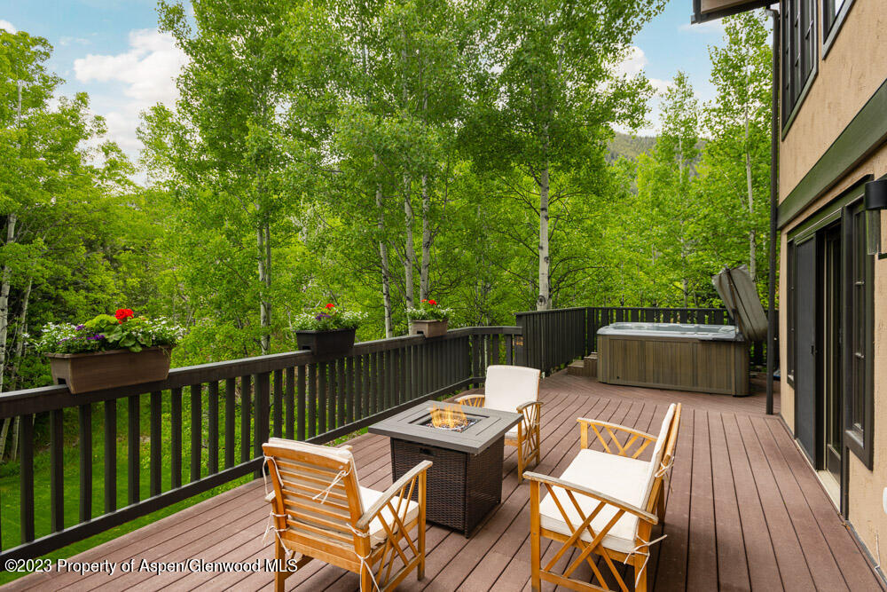 Furnished outdoor deck with a fire table and hot tub, overlooking dense green trees.