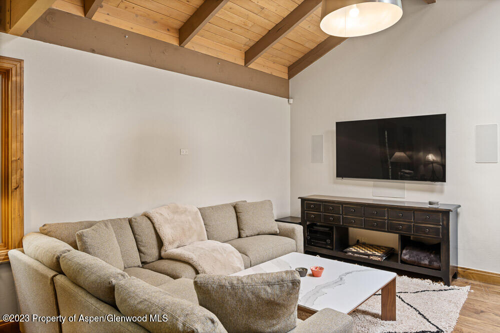Living room with a beige sectional beneath a vaulted wood ceiling and a television on the wall.