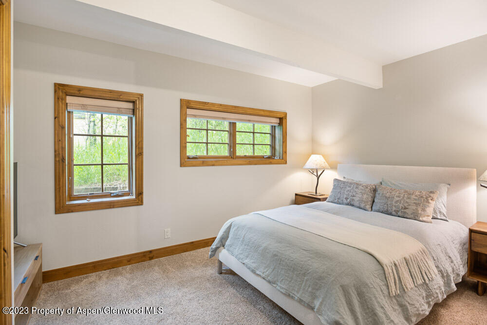Bedroom with a white bed and gray bedding beneath two wood-trimmed windows.