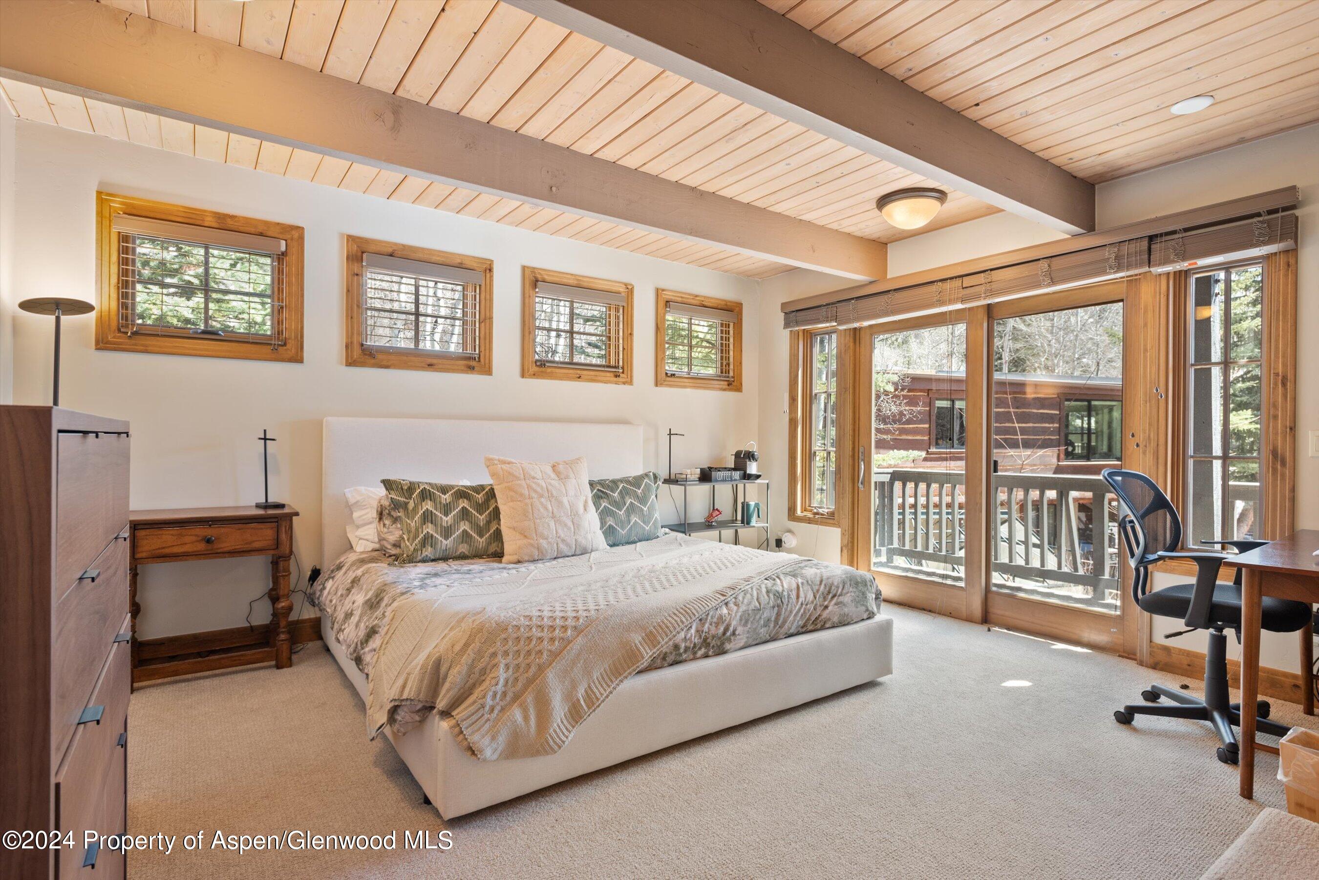 Bedroom with a large bed, exposed wood ceiling beams, and glass doors opening onto a deck.