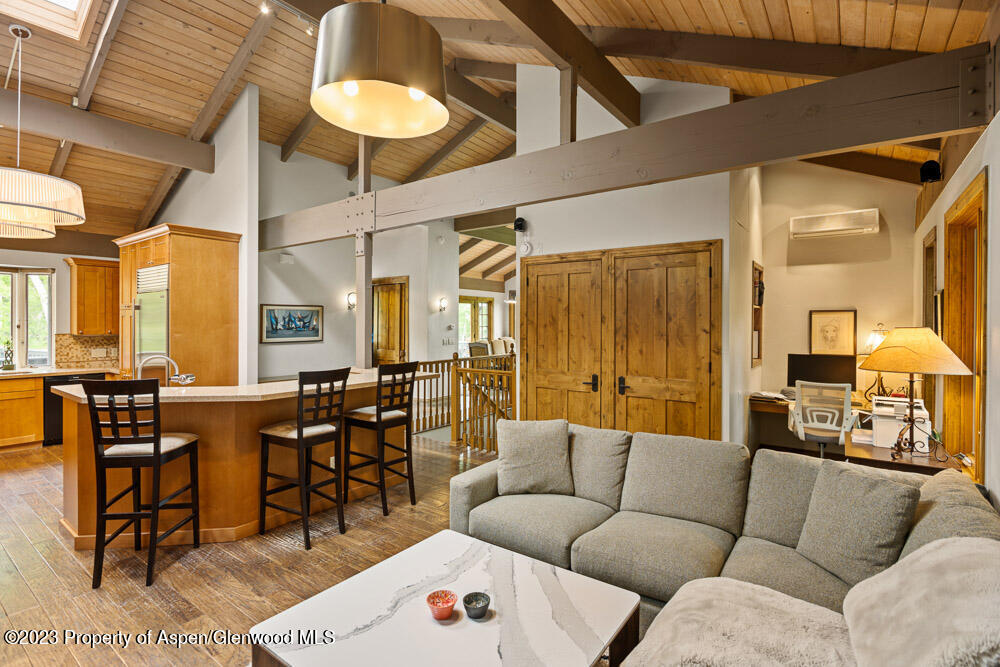 Open-plan living room and kitchen with a gray sectional, island seating, and vaulted wood ceiling.