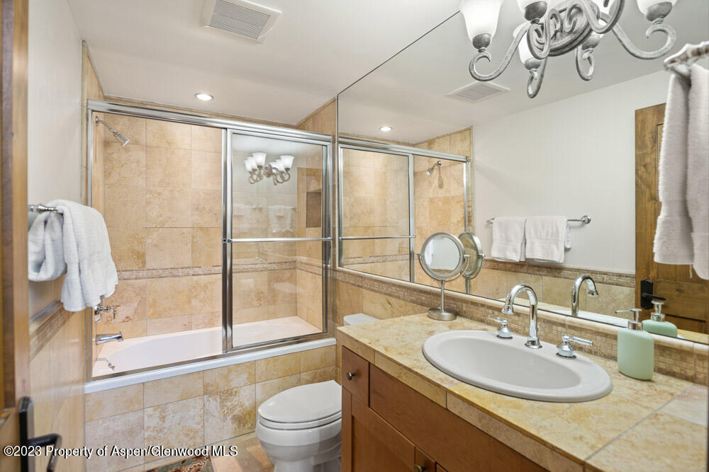 Bathroom with a glass-enclosed tub and shower, beige stone tile, and a matching vanity countertop.