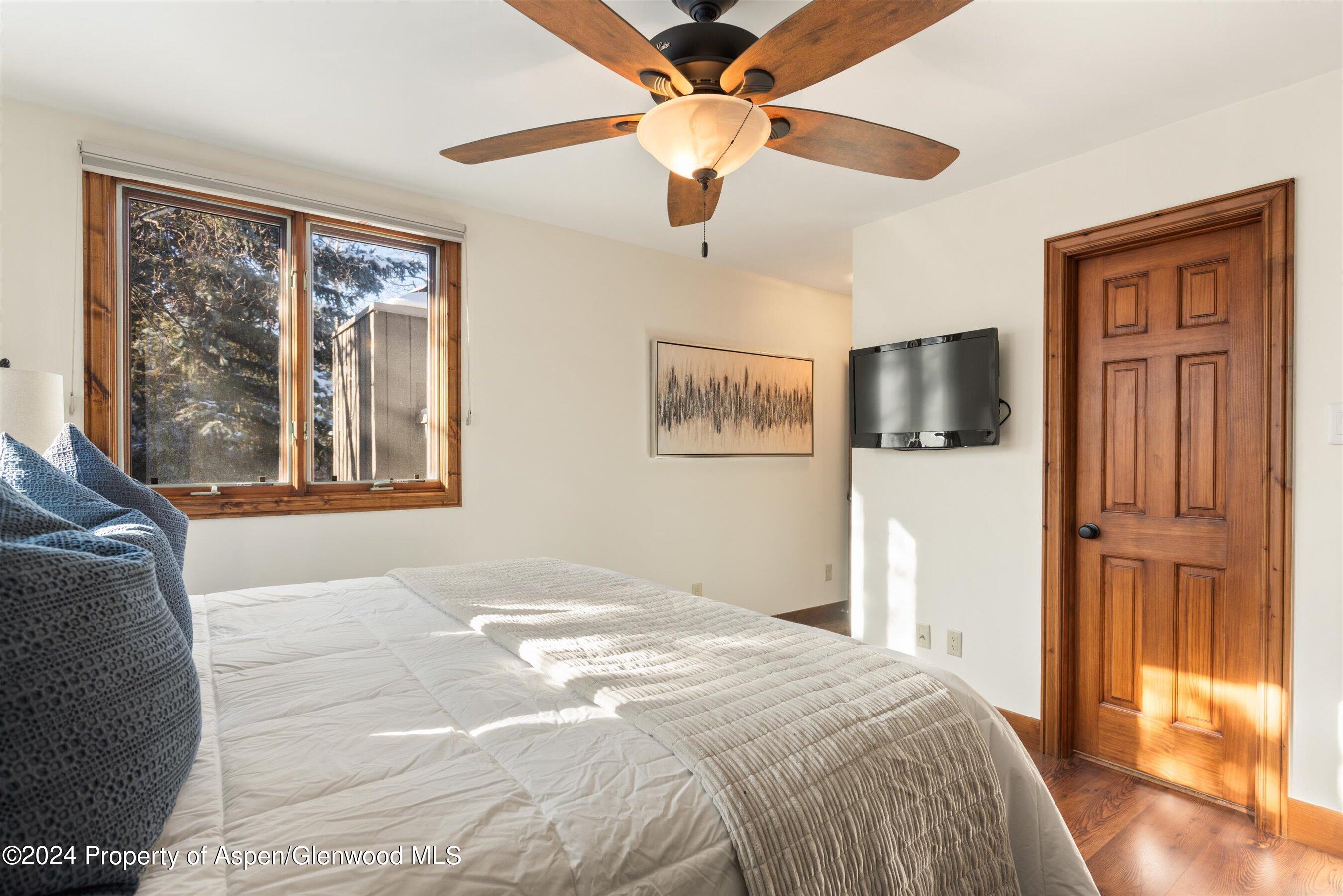Bedroom with a large bed, wood-trimmed windows, ceiling fan, and paneled wood door.
