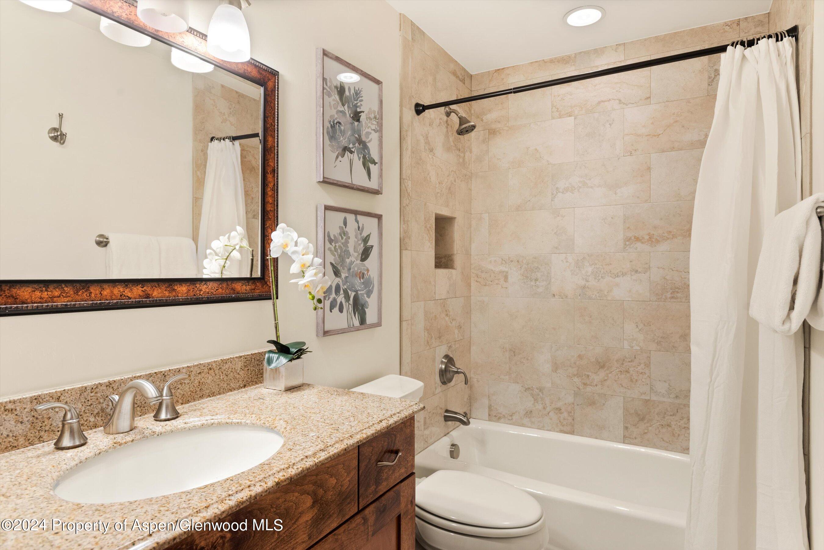 Bathroom with granite vanity and sink beside a stone-tiled bathtub with white curtain.