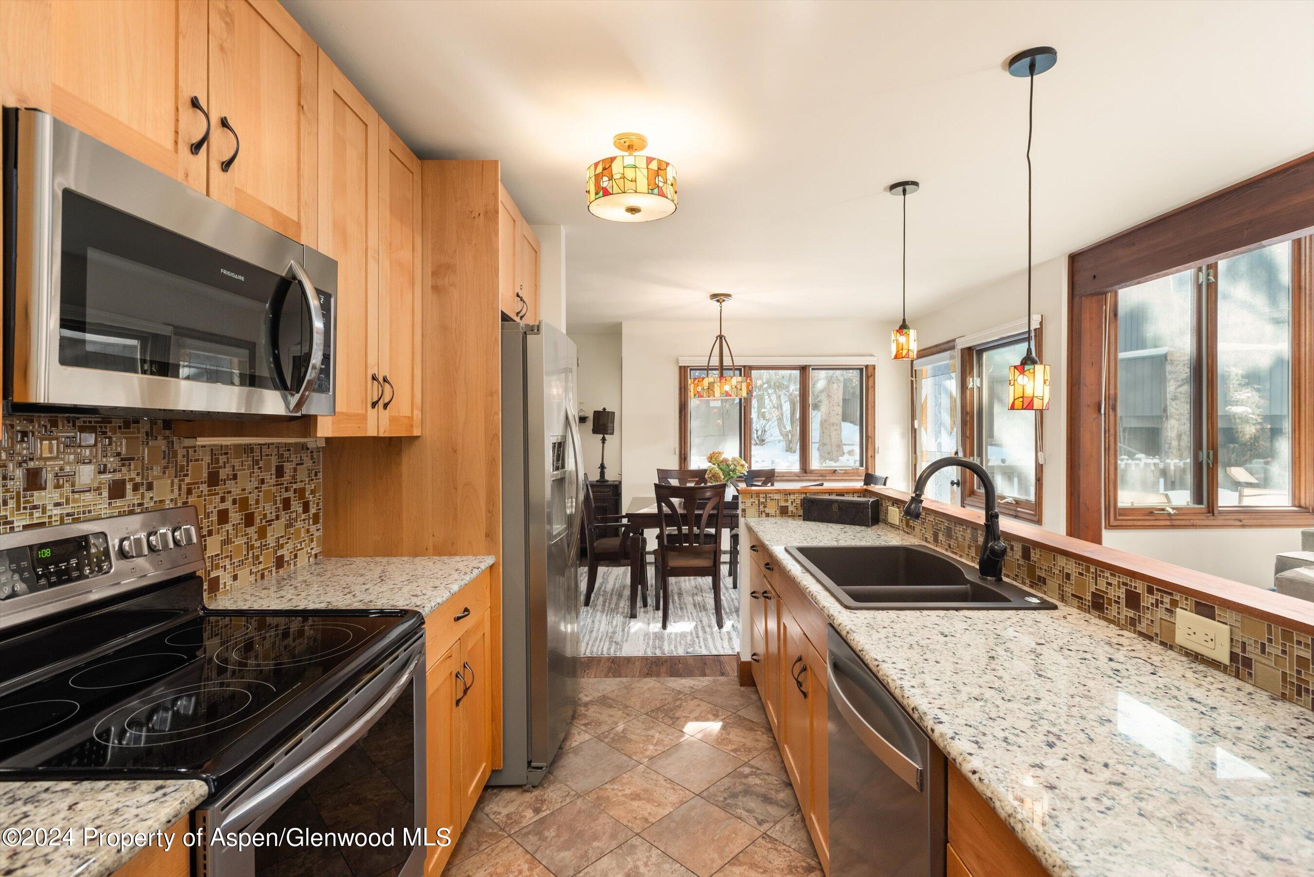 Kitchen with maple cabinets, granite counters, mosaic backsplash, and dining table beside snowy windows.