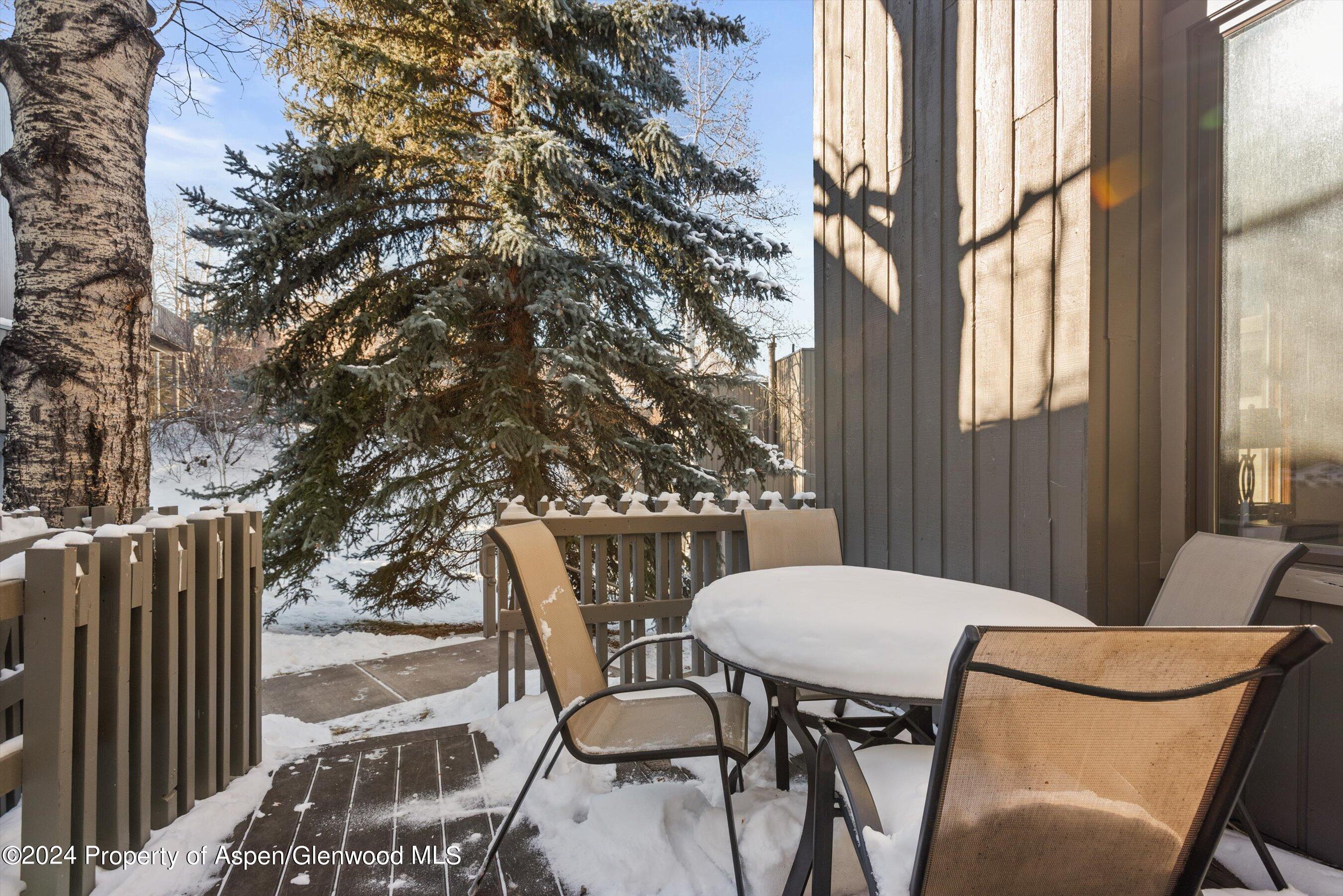 Snow-covered deck with a patio table and chairs beside a snow-dusted evergreen.