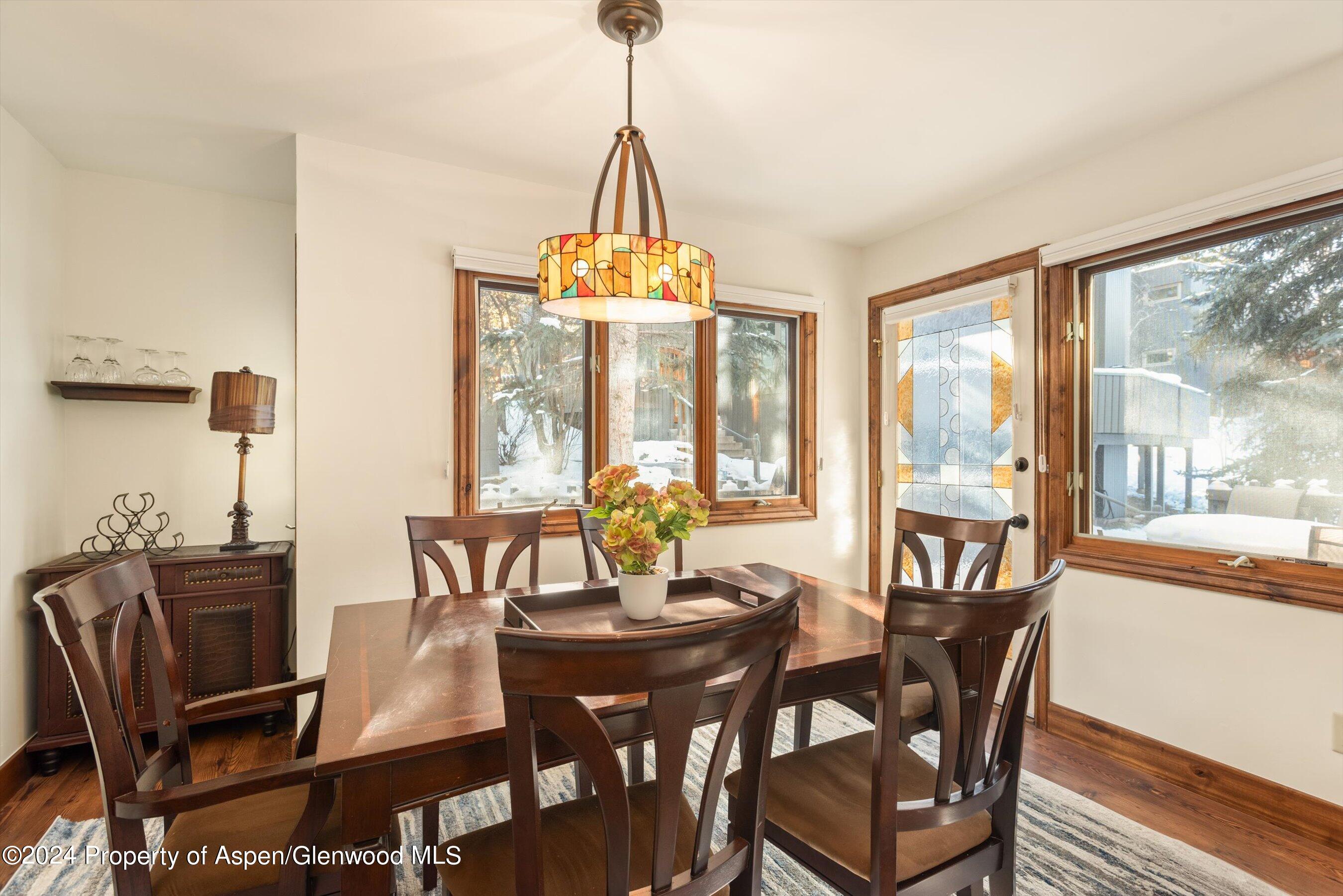 Dining room with a dark wood table, colorful pendant light, and windows overlooking a snowy yard.