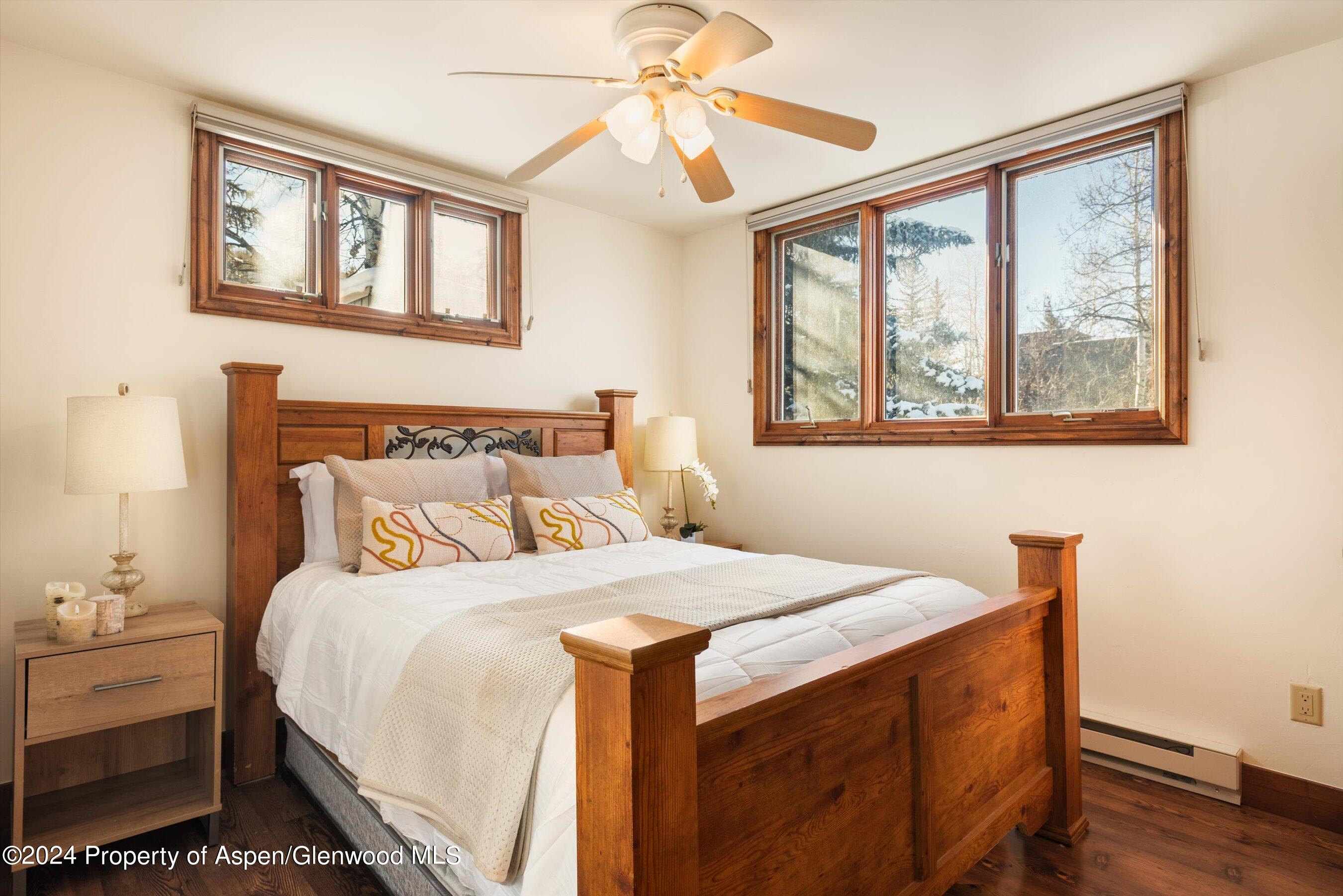 Bedroom with a wooden bed and white bedding, overlooking snow-covered trees through wood-framed windows.