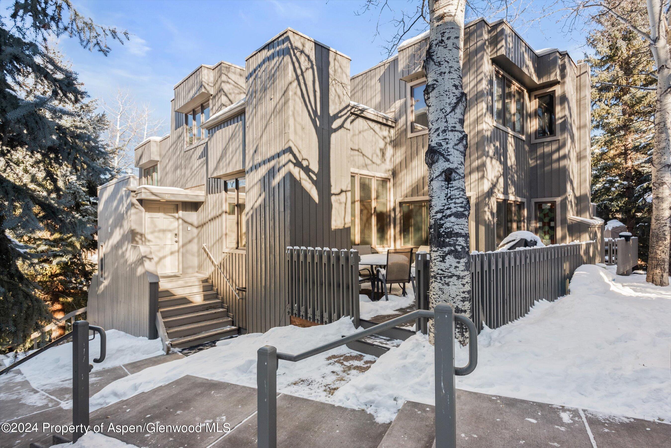 Multi-story gray home with a fenced patio and snow-covered grounds among trees.