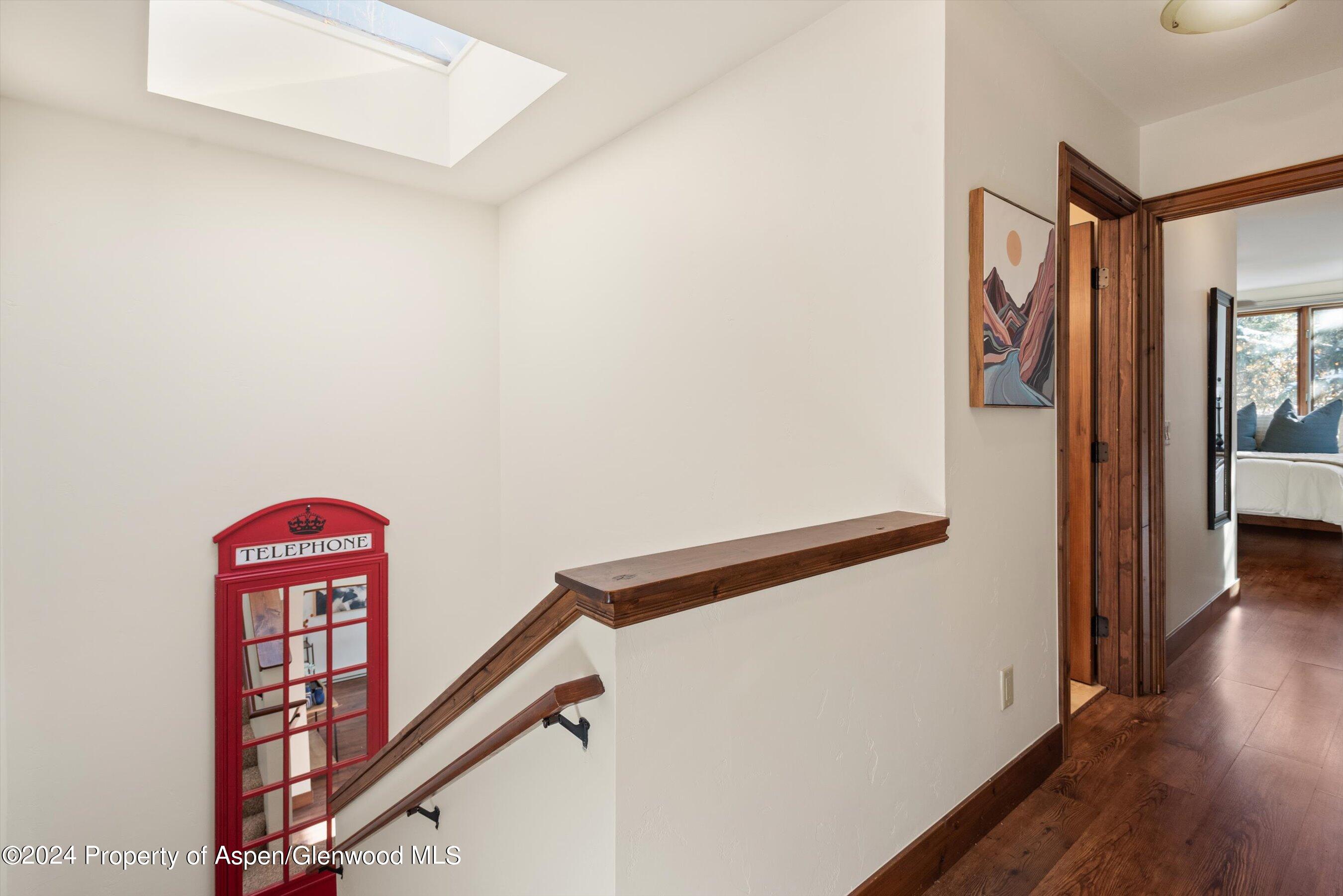 Stair landing with a skylight, dark wood railings, and a red telephone-booth-style mirror.