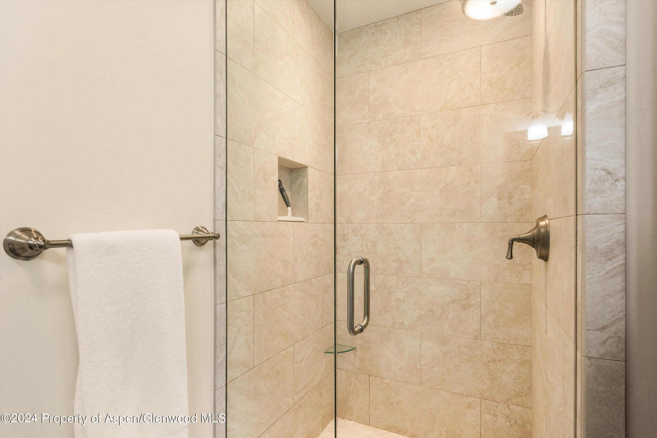 Tiled walk-in shower with a glass enclosure, recessed shelf, and white towel.