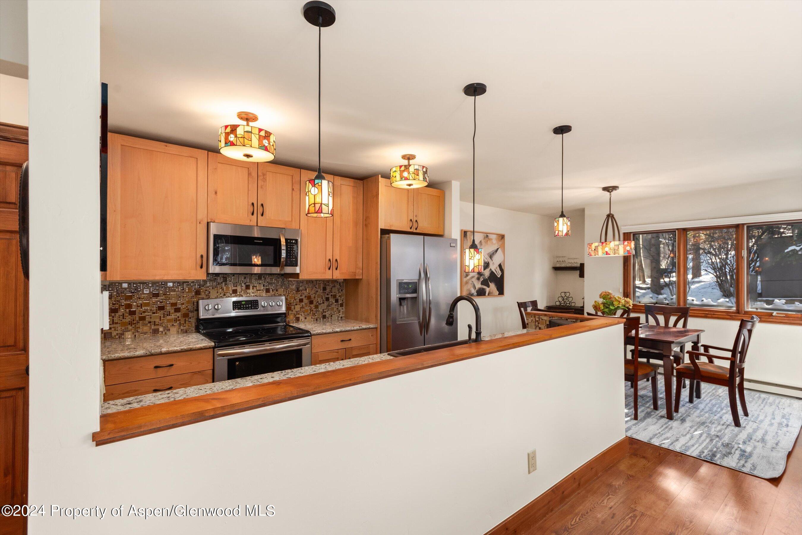 Kitchen with warm wood cabinets and stainless appliances opening to a dining area beside a snow-covered view.