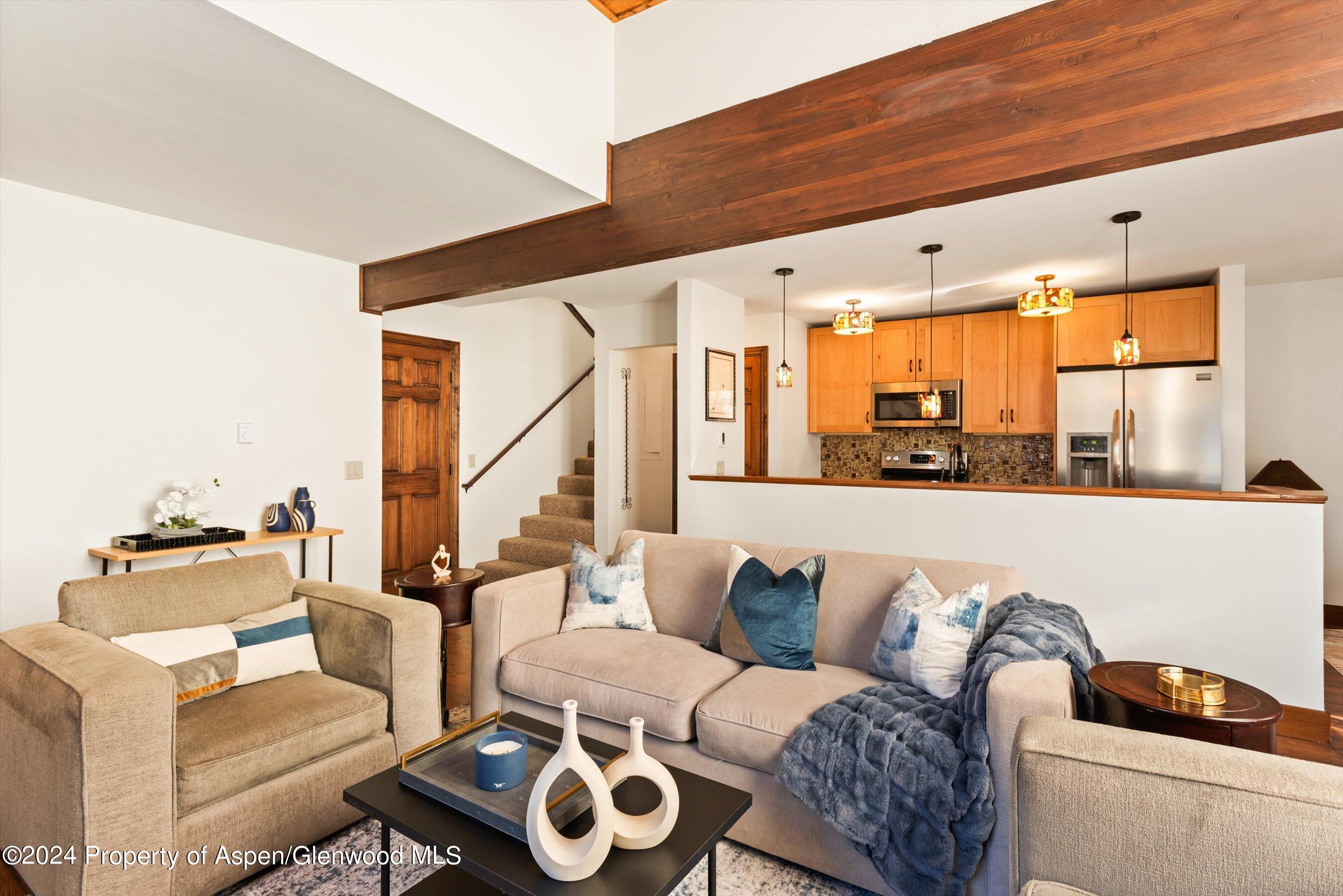 Staged living room with a large exposed wood beam and open kitchen.