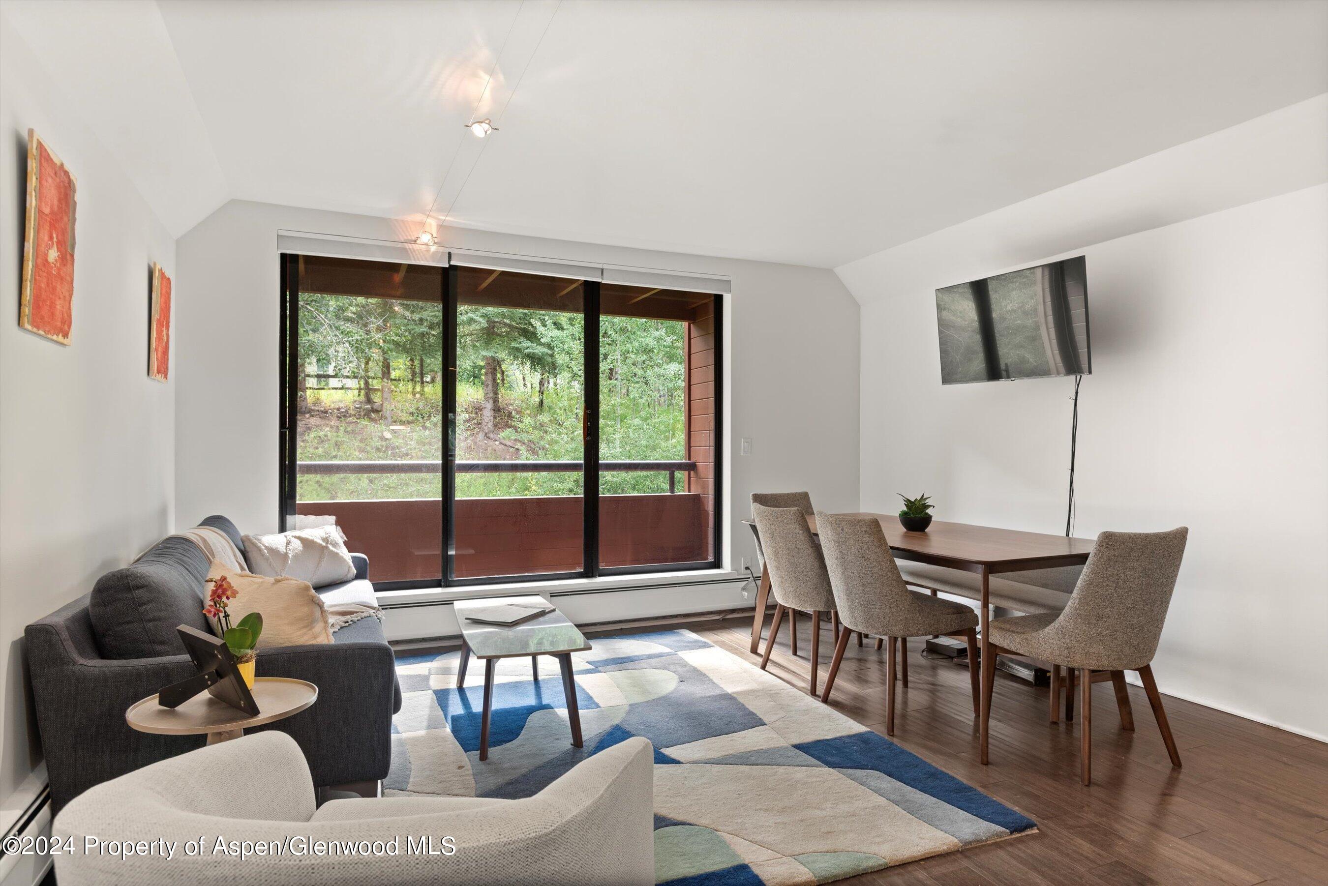 Furnished living and dining area with sliding doors opening onto a tree-lined balcony.