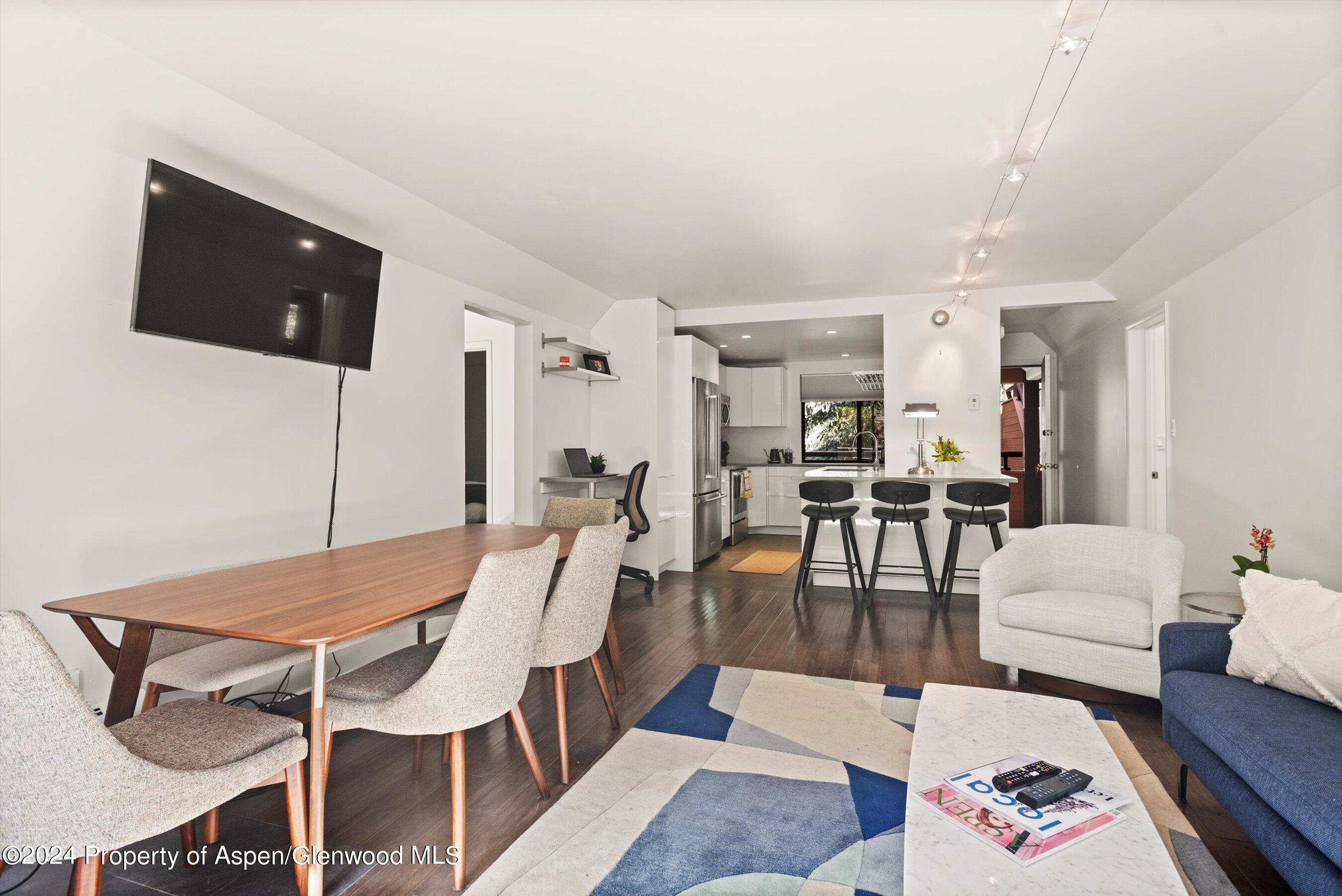 Open-plan living and dining area with a wooden table, geometric rug, and kitchen island with three stools.