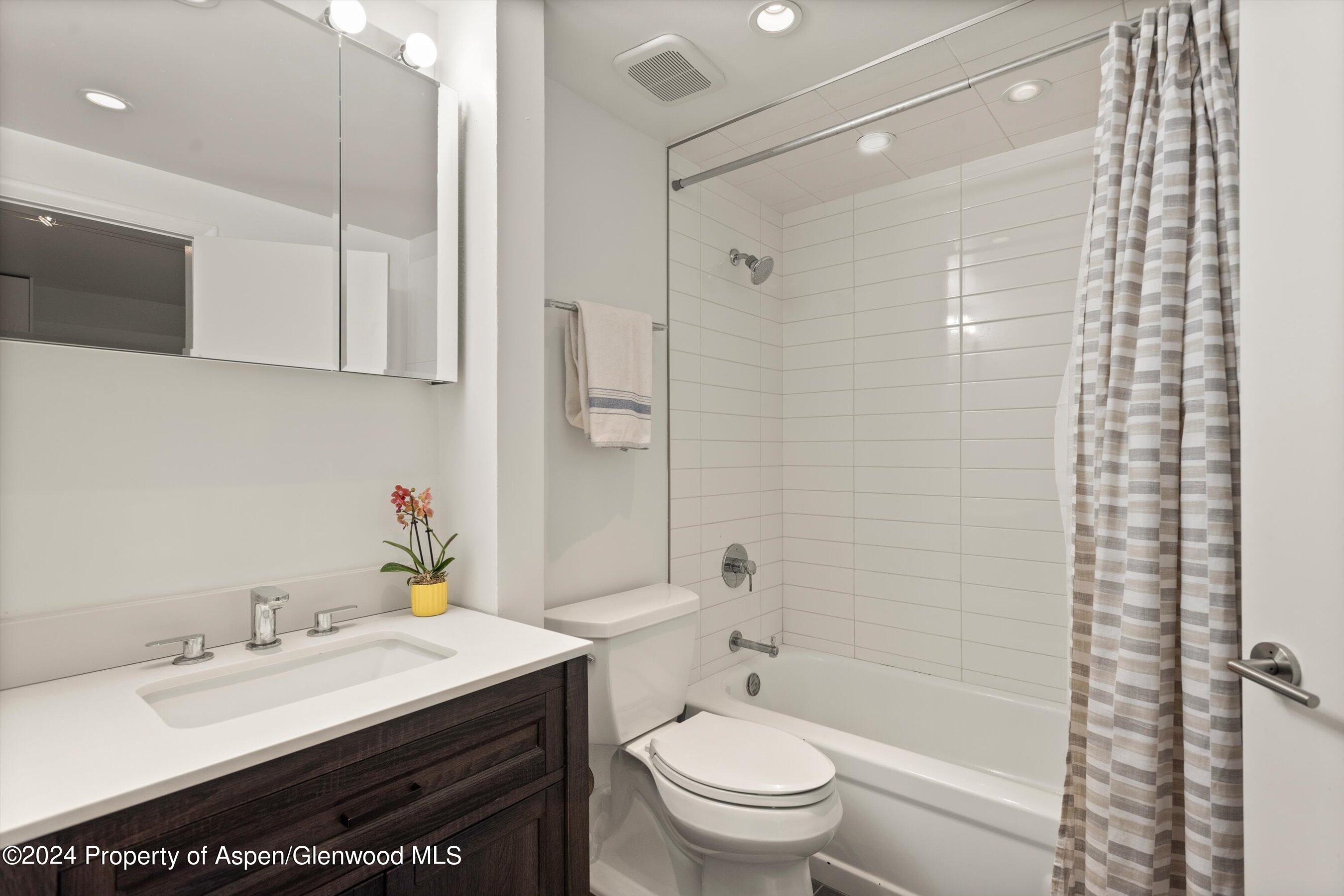 Bathroom with a white vanity, dark wood drawers, and a tub with white tile surround.