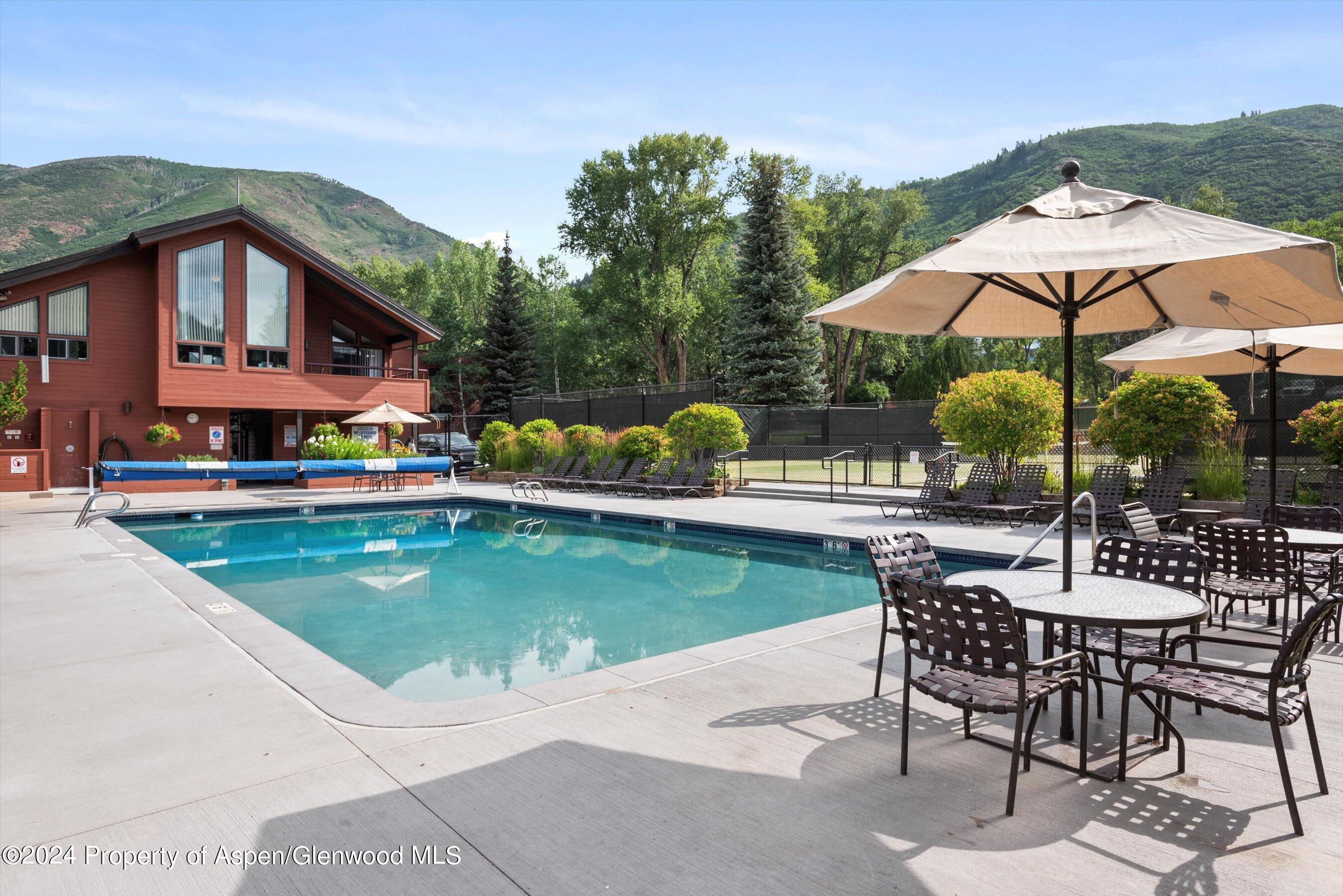Outdoor pool beside a red-sided building, with patio seating and green mountain views.