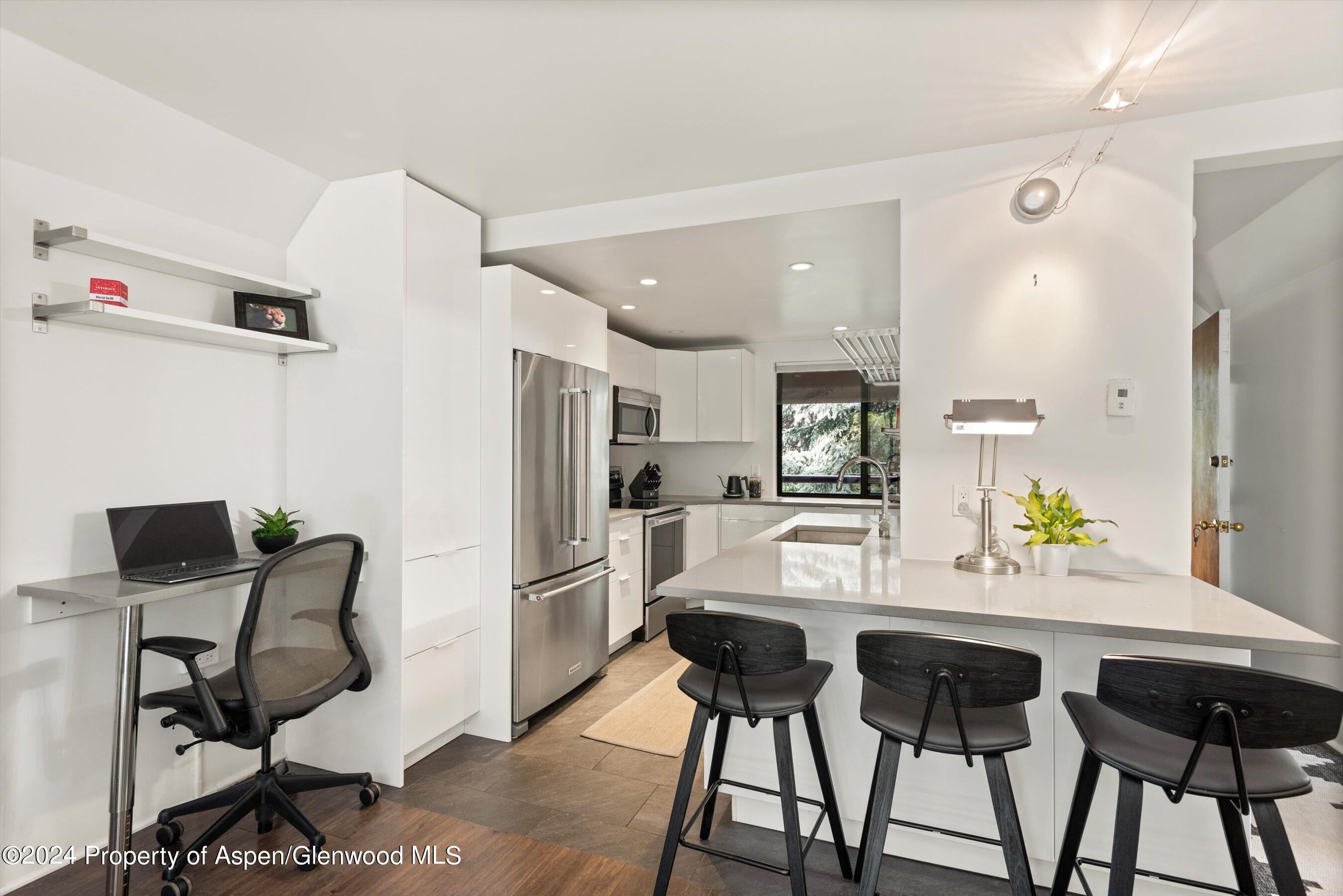 Modern white kitchen with stainless appliances, a large island, and a compact desk nook.